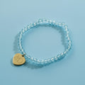 Blue beaded bracelet with a gold heart-shaped charm on a light gray background