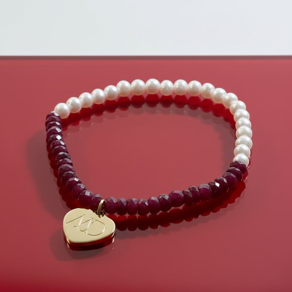 Bracelet with white pearls, red beads, and a gold charm on a light gray background