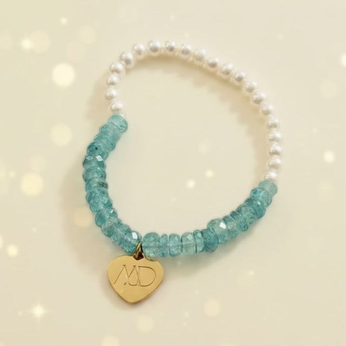Bracelet with white pearls and blue beads featuring a gold heart charm on a light gray background