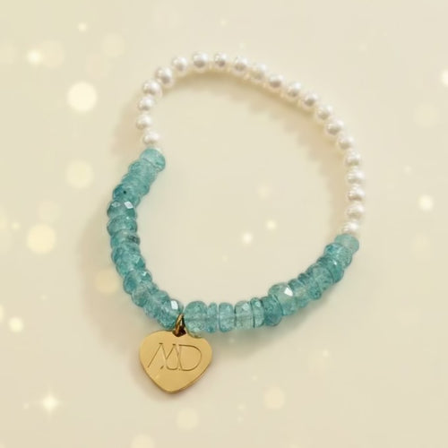 Bracelet with white pearls and blue beads featuring a gold heart charm on a light gray background