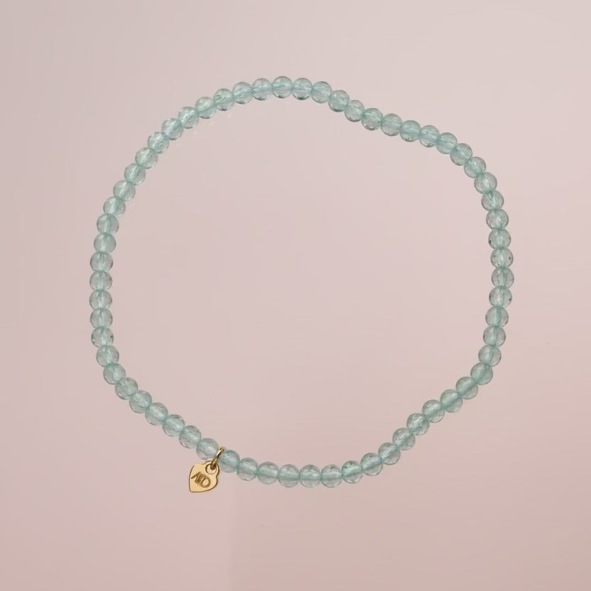 Turquoise beaded bracelet with a gold clasp on a beige background