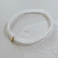 White beaded bracelet with a gold charm on a light gray background