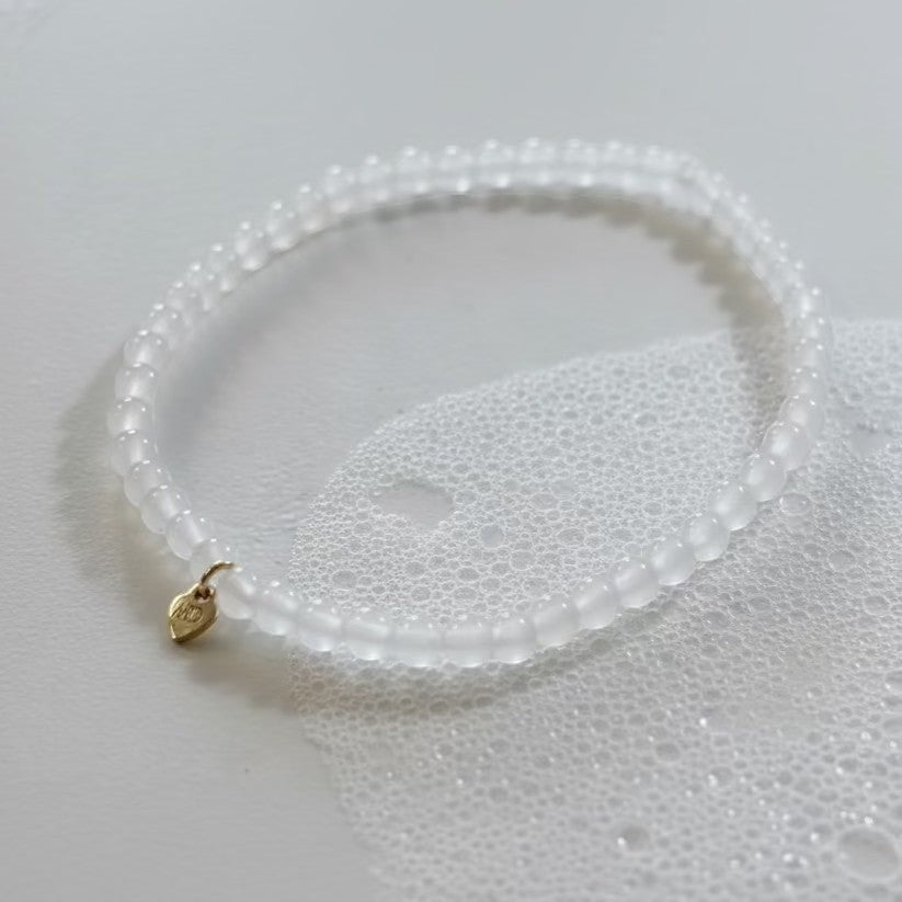 White beaded bracelet with a gold charm on a light gray background