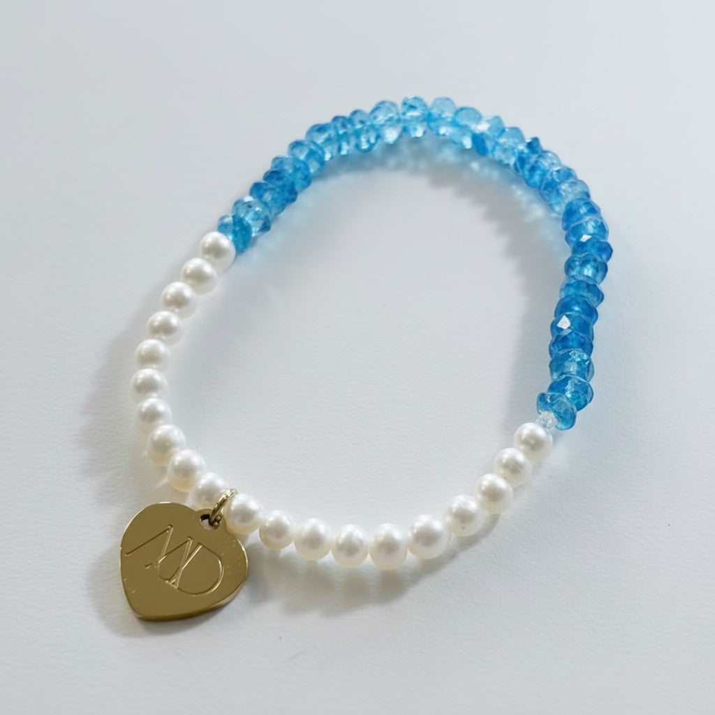 Bracelet with blue and white beads and a gold heart-shaped charm on a light gray background