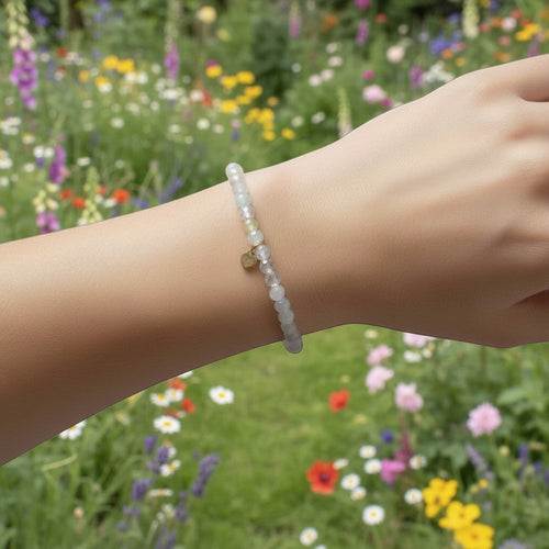 The Mermaid's Den Astilbe Morganite beaded bracelet with a small gold charm worn on a wrist in a flower garden.