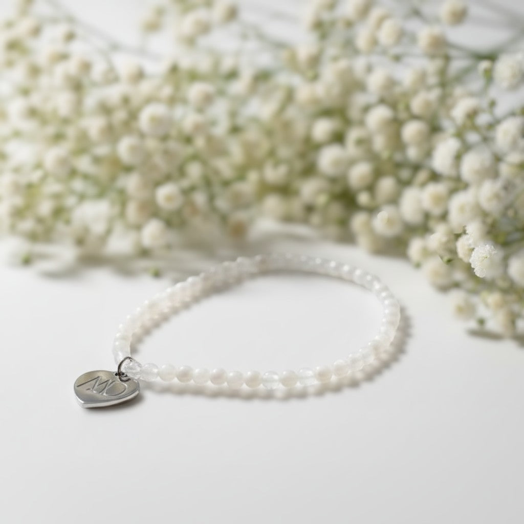 The Mermaid's Den Gypsophilia White Moonstone beaded bracelet with a silver heart charm against baby's breath flowers.