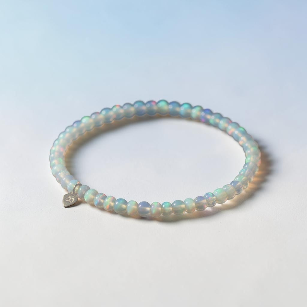 The Mermaid's Den Hyacinthus White Opal beaded bracelet with a small heart charm, featuring iridescent gemstone beads.