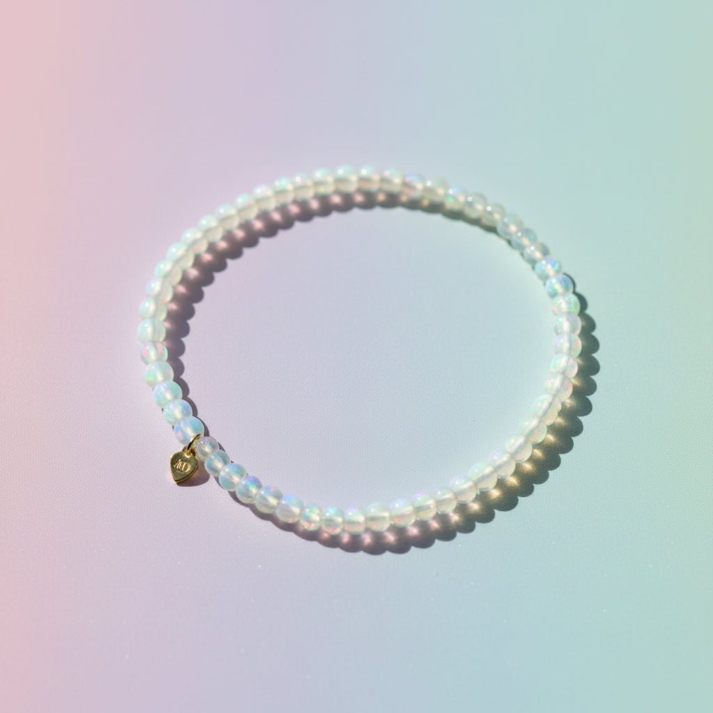 The Mermaid's Den Hyacinthus White Opal beaded bracelet with a small gold heart charm on a neutral background.